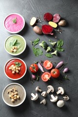 Different tasty cream soups in bowls and ingredients on dark grey table, flat lay