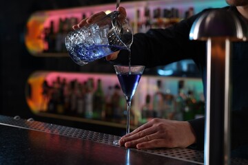 Bartender making fresh alcoholic cocktail at counter in bar, closeup