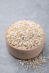 Raw barley groats in bowl on grey table, closeup