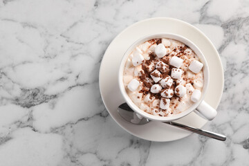 Cup of aromatic hot chocolate with marshmallows and cocoa powder served on white marble table, top...