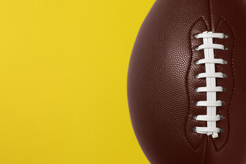 American football ball on yellow background, top view. Space for text