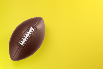 American football ball on yellow background, top view. Space for text