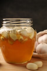 Honey with garlic in glass jar on wooden table, closeup
