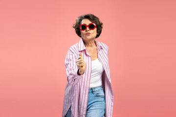 Happy funny modern grandmother wearing stylish pink shirt, sunglasses  dancing having fun isolated on pink background. Freedom, positive lifestyle concept - obrazy, fototapety, plakaty