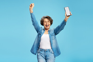 Overjoyed senior woman holding mobile phone with mockup, win something celebration success isolated...