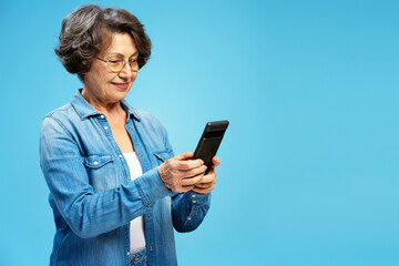 Portrait smiling gray haired senior woman holding mobile phone shopping online, reading text message isolated on blue background. Technology concept 