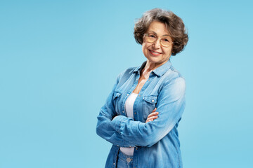 Portrait confident smiling senior woman, happy modern grandmother wearing casual clothing holding arms crossed isolated on blue background, copy space 