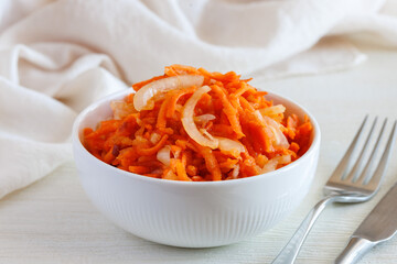 Fresh healthy vegetarian carrot salad with apple, onion and spices in the bowl with fork and knife. Side view, close up