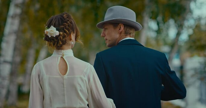 married couple in gowns of 19th century walking in park in autumn day, rear view, 4K, Prores