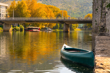 Obraz premium Golden autumn landscape in historical tourist city with bridge Trebinje Bosnia and Herzegovina snow-free cityscape, boat near ancient stone fortress, reflected in surface of river, yellow trees Balkan