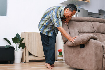 Old Asian man having problem with leg pain, leaning on the couch at home