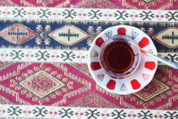 Red Turkish tea with traditional pear shaped glass on patterned tablecloth in cafe