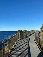 Fototapeta premium Boardwalk to the beach. Wooden bridge over the sea. Walkway near the blue turquoise ocean, waves. Pier in the sea. Wood fence.