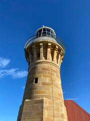 Lighthouse on the island at daytime. Sandstone lighthouse at the top of a hill. Coast ligthouse against a blue sky. Lighthouse in the harbor. Lighthouse on the coast of the region sea.