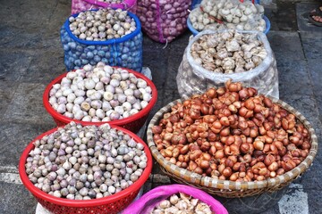 Baskets and bowls filled with onions, shallots and garlic cloves for sale at an outdoor market in Southeast Asia