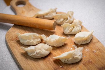 Fototapeta na wymiar Process of making chinese dumplings. Raw dough and rolling pin on wooden chopping board.