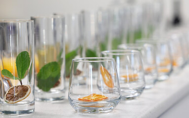Clean glass tumblers or drinking glasses with dried dehydrated citrus fruit slices inside with mint leaves ready for a cocktail or mocktail to be poured in.