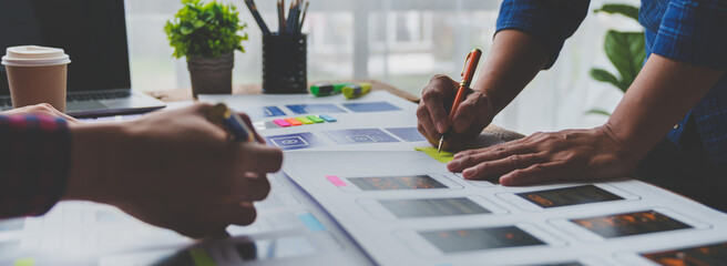 ux developers and ui designers brainstorm on tabletop mobile app layout design planning design color coding at modern office Creative digital development agency. - obrazy, fototapety, plakaty