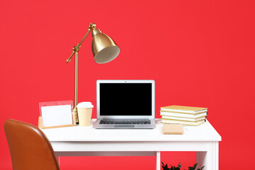 Stylish workplace with modern laptop and lamp on red background