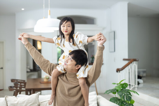 Young father playing with cute daughter sitting up on neck to fly like plane open arms leisure hobby, Asian happy family having fun at home, Girl sitting on father back, endless imagination.