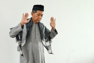 Elderly Asian muslim man praying, raising hands and doing first movement in salat or takbiratul...