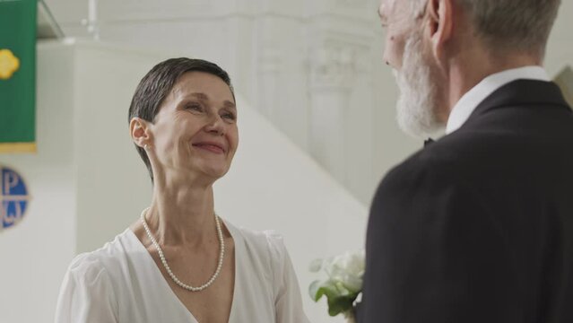 Medium shot of Caucasian adult couple in love making final preparations before start of church wedding ceremony. Beautiful bride adjusting suit and buttonhole of her groom, looking at him and smilingM