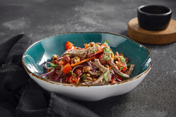 Rustic Georgian-style beef salad with beans, tomatoes, nuts, and red onion, served in a ceramic bowl on a dark surface