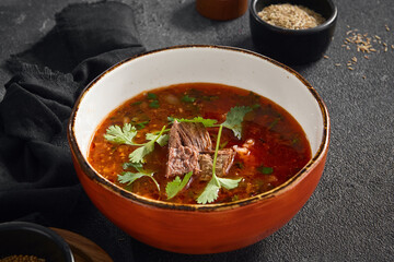 Authentic Georgian Harcho soup, rich with beef and fresh cilantro leaves, served in a rustic orange bowl on a dark grey surface.