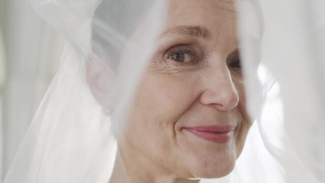 Closeup portrait of beautiful mature Caucasian bride wearing white veil looking at camera before wedding ceremony
