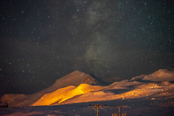 The Milky Way visible over the yellow-lit mountains of Antarctica - obrazy, fototapety, plakaty