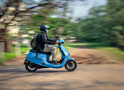 Slow shutter, Motion blur image of a rider wearing helmet for safety, riding on a blue electric moped.