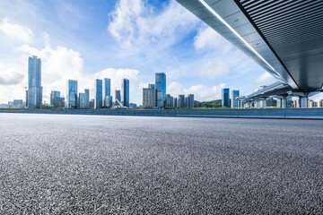 Asphalt road and pedestrian bridge with city buildings under blue sky