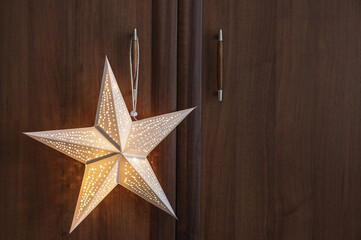 A glowing paper Christmas star hangs on the handle of a wooden cabinet. Christmas interior..Copy...