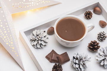Cozy winter arrangement with a white tray with coffee and chocolate and a paper Christmas star on the windowsill.