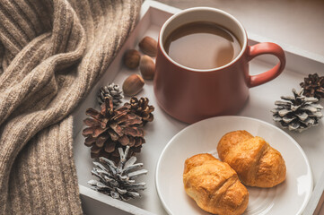 White tray with coffee and croissants and a knitted scarf on the windowsill. Cozy winter composition.