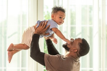 Happy african black parents dad father throw baby son on piggyback and neck riding teasing fun near...