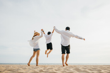 Family outdoor activities, Back family mother, father and son holding hands and jumping in air at dawn time, Happy Asian family people have fun together on beach on holiday summer vacation travel