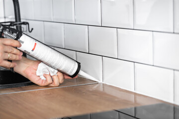 master of interior decoration, smears the joint of the tile and the kitchen countertop with white...
