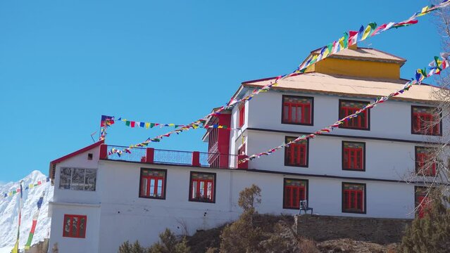 4K shot of prayer flags waving in front of the Shashur Monastery near Keylong in Lahaul Valley, Himachal Pradesh, India. Flags waving in front of the monastery against the blue sky during winter.