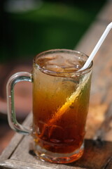 Es Teh. iced tea is a fresh drink made from tea, water, sugar, and ice cubes. iced tea in a clear glass on a brown wooden table. Indonesian drink. 