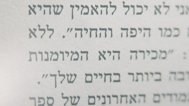A macro smooth and detailed tilt up shot of a book in Hebrew, black letters on white paper, 4K video