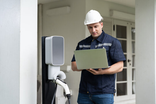 Qualified Technician Working On Home EV Charging Station Installation, Making Troubleshooting And Configuration Setup On Charging System With Laptop For EV At Home. Synchronos