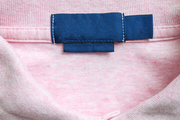 Blank blue laundry care clothes label on pink shirt fabric texture background