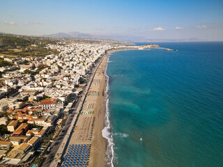 Aerial view of Rethymno beach in Crete, Greece, organized beautiful beach with umbrellas, touristic area and beach hotels
