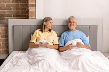 Fototapeta premium Happy senior couple sitting, drinking coffee and talking together in their bed.