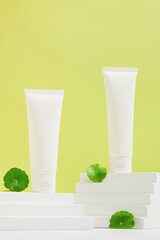 Two unlabeled cosmetic tubes are placed on two white platforms on a pastel background with fresh...