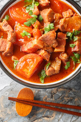Babi masak tomat is a traditional Indonesian dish made with a combination of pork, tomatoes, onion, garlic, lemongrass, and a spice paste closeup in the bowl on the table. Vertical top view from above