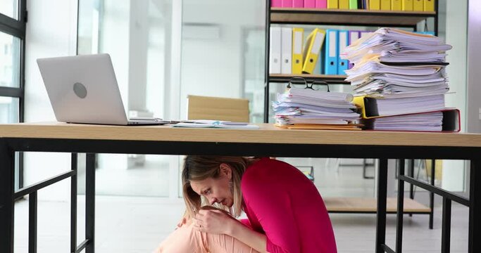 Frightened young woman hiding under office desk during earthquake