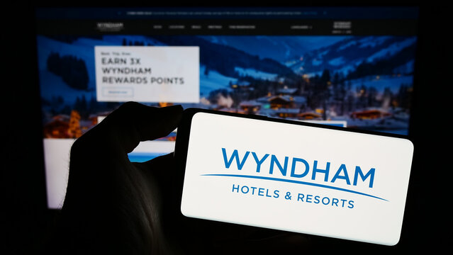 Stuttgart, Germany - 11-29-2023: Person holding smartphone with logo of US hotel company Wyndham Hotels and Resorts Inc. in front of website. Focus on phone display.