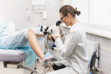 woman doctor look microscope at gynecologist's appointment. Female gynecologist examining patient on chair with equipment. Colcoscopy and Pap test - obrazy, fototapety, plakaty